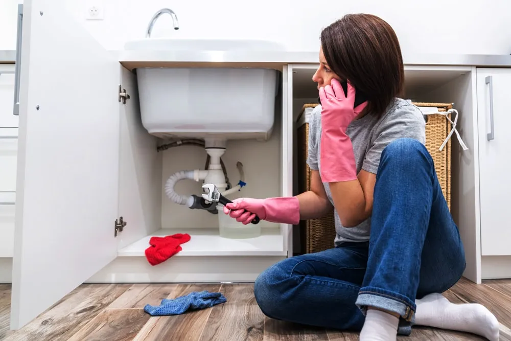 woman-sitting-near-leaking-sink-sking-help-by-phone-min.jpg